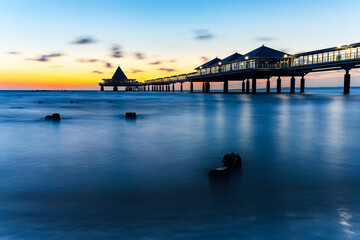 The longest wooden pier in Germany on the Baltic Sea, Heringsdorf Pier at sunrise with colorful wooden breakwaters. There is a restaurant at the end of the pier.