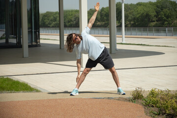 Sportsman doing exercise while working out on city outdoors. Fit brunette man wearing sports casual...