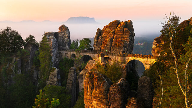 Rock formation with the Bastei Bridge in Saxon Switzerland at sunrise with fog in the background. A well-known tourist destination in Germany.