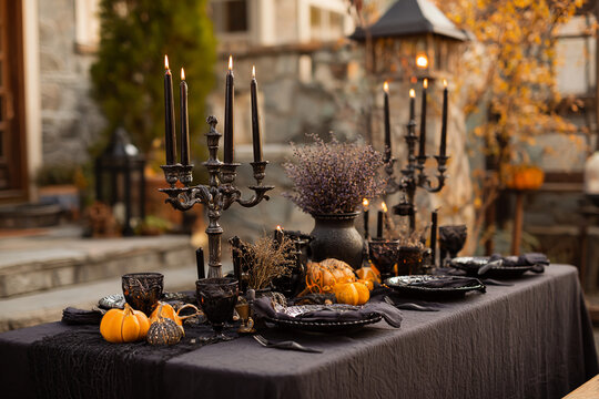 Outdoor evening Halloween dinner table with black tablecloth, antique dishes, candelabra, dried flowers, and mini pumpkins, smoke from extinguished candles creating soft haze - Powered by Adobe
