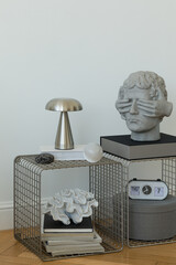 Detailed view of minimalist side table with modern sculpture, books and metallic lamp. Design and curated styling.