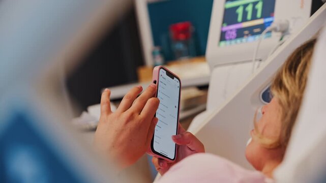 Chisinau, Moldova - May 31, 2025: Pregnant woman using the iHerb app on her phone while doing a prenatal check-up at the doctor's office