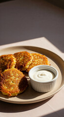 Golden Potato Fritters with Sour Cream on Beige Plate