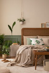 Warm and cozy bedroom interior with mock up poster frame, boho bed, beige bedding, green wall with stucco, books, brown slippers, plants in pots and personal accessories. Home decor. Template.