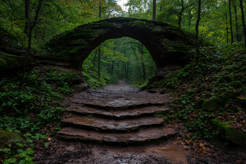 Stone archway over path, lush forest scene.  A natural, moss-covered tunnel creates a unique passage.  Nature's artistry shines through!