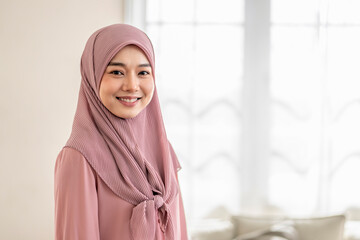 portrait happy young muslim woman in hijab looking to camera while staying indoor at home