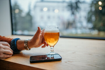 Man drinking beer in a pub and using smartphone by the window