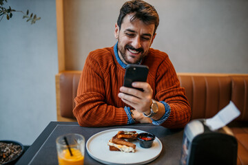 Happy man using smartphone while having breakfast in cafe