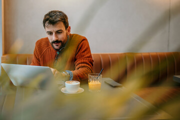 Focused freelancer working on laptop in cafe with cappuccino and juice
