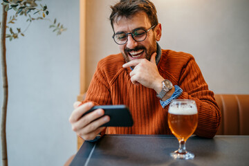 Happy man using smartphone and drinking beer in restaurant