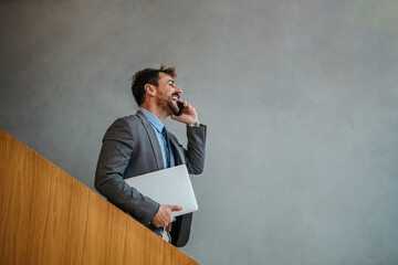 Businessman walking and talking on phone holding laptop