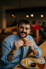 Happy businessman eating burger and french fries in restaurant