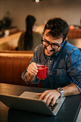 Freelancer working on laptop and talking on phone in cafe, drinking juice