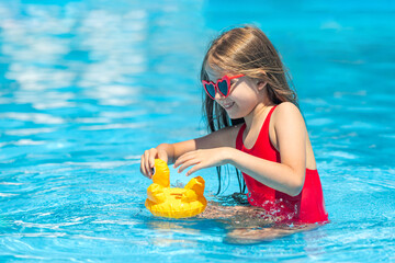 Side view happy little girl in red swimsuit has fun on vacation at the hotel pool. Summer outdoor activity during family vacation in tropical resort. Beach and water children toys. Sun protection.