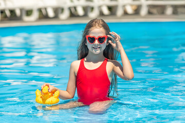 Front view happy little girl in red swimsuit has fun on vacation at the hotel pool. Summer outdoor activity during family vacation in tropical resort. Beach and water children toys. Sun protection.