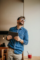 Happy freelancer holding tablet and laughing in cafe