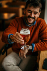 Happy man raising glass of beer in celebration at pub