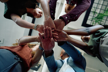 Directly below closeup of diverse business people stacking hands in office during daytime
