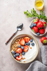Natural greek yogurt with granola, blueberry and strawberry in a bowl on a light background