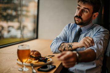 Businessman waiting impatiently at restaurant table, rolling up sleeve and checking time