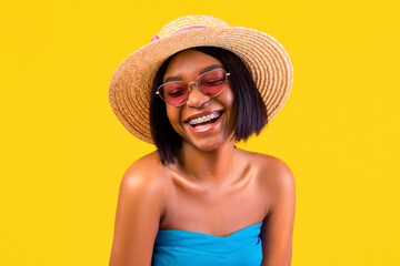 Portrait of happy African American lady in elegant dress, straw hat and sunglasses laughing on...