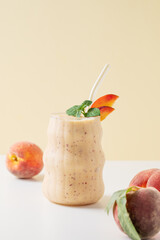 Smoothie with peach and banana in a glass on a yellow white background with tropical fruits.