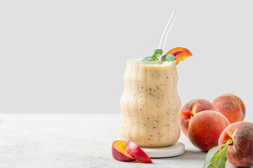 Smoothie with peach and banana in a glass on a marble stand on a light background with tropical fruits
