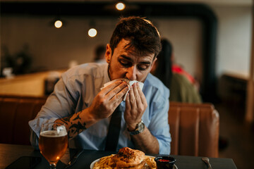 Businessman wiping his mouth while enjoying burger and beer in restaurant