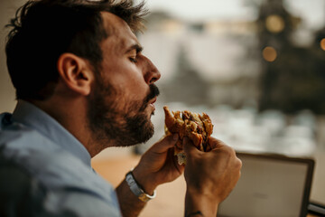 Businessman enjoying tasty burger during lunch break in office
