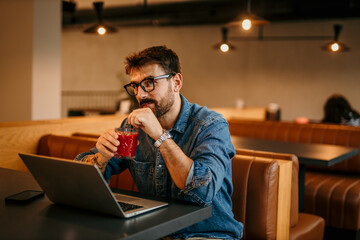 Thoughtful freelancer drinking juice and working on laptop in cafe