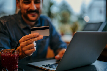 Smiling freelancer doing online shopping using credit card and laptop in cafe