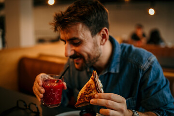 Happy customer enjoying sandwich and juice in restaurant