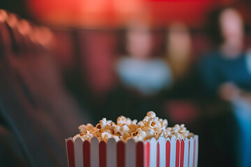 Movie snack: A bucket of popcorn with red and white stripes sits in a dark theater, ready for the film to begin. Sweet or salty, a perfect film accompaniment.