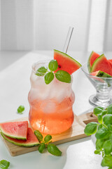Watermelon mojito cocktail with ice and mint in a glass on a wooden board on a white table