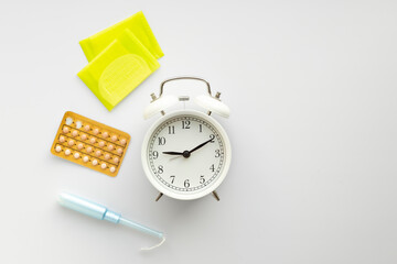 Flat lay of alarm clock, tampon, pads, birth control pills on white.