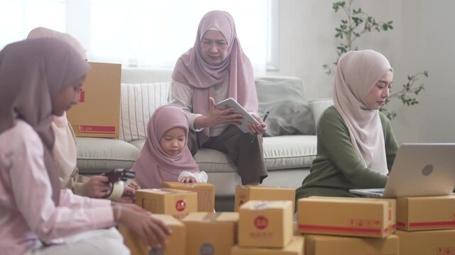 Muslim big family working together on online business packing parcels for shipping using laptop at home, halal brand startup teamwork, delivery, e-commerce with family and SME, muslim entrepreneurship