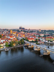 Obraz premium Early morning light bathes the historic city of Prague, illuminating the medieval architecture. The Charles Bridge spans the calm Vltava River, enhancing the tranquil panorama.