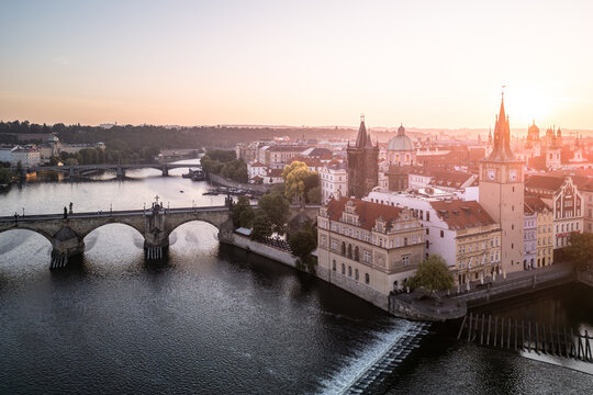 Morning light casts a warm glow over Charles Bridge in Prague, highlighting the architecture and the tranquil Vltava River. The old town awakens softly, free of crowds.