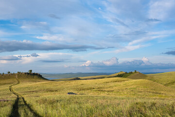 Beautiful sunset light in the evening, in a hilly steppe area in Siberia. A car in a field in the middle, the sky in the clouds