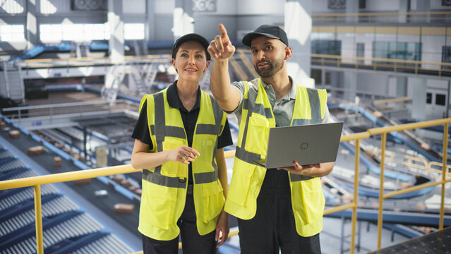 Delivery Station Warehouse Associates Using Laptop Computer to Manage the Automated Conveyor Belt Load, Prepare Online Shopping Orders for Delivery. Young Diverse People Working at a Logistics Center
