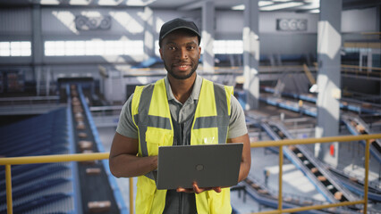 Black Employee Working at a Modern Logistics Center for an International Online Shopping Website. Portrait of a Happy Smiling African Man Using a Laptop Computer and Looking at Camera