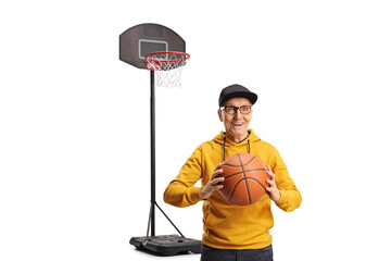 Smiling elderly man with a ball in front of a basketball hoop