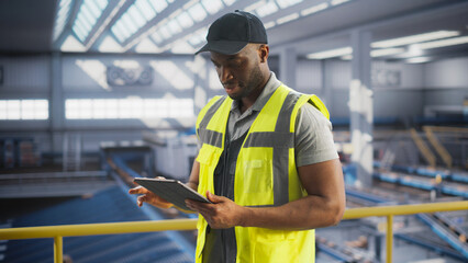 Black Employee Working at a Modern Logistics Center for an International Online Shopping Platform. African Man Using a Laptop Computer to Optimize the Orders Before Deliveries