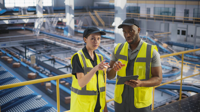 Delivery Station Warehouse Associates Having a Conversation at a Modern Logistics Center. Workers Using Tablet to Manage the Automated Conveyor Belt Load, Prepare Online Shopping Orders for Delivery