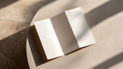 Naklejka premium Blank tri fold brochure mock up, white paper on light stone table with sunlight shadows. Minimalist marketing flyer design. Cloud Dancer Color of the Year 2026
