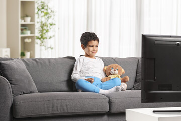 Little boy sitting on a sofa with a teddy bear and a dog