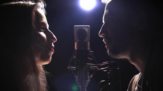 A man and a woman in a studio dubbing a film, record own voices on microphone