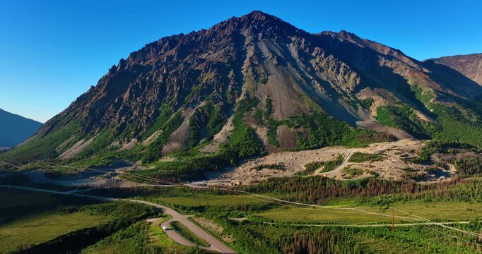 Huge bare rock with scarce vegetation on the slopes. Footage above the valley crossed by the highway and electricity line. Alaska landscapes.