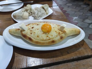 Adjarian khachapuri with eggs on the yellow plate. Traditional georgian pastry - adjarian khachapuri with cheese and raw yolk. Khachapuri with egg on yellow background in rustic style. 