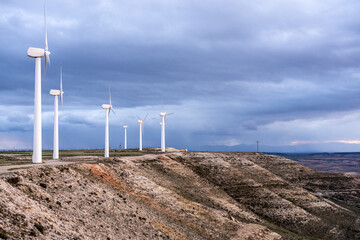 Elevated view of wind turbines along a rugged landscape in Zaragoza, Spain, combining topographic contrasts, cloudy atmosphere and the rhythm of sustainable infrastructure across hills.